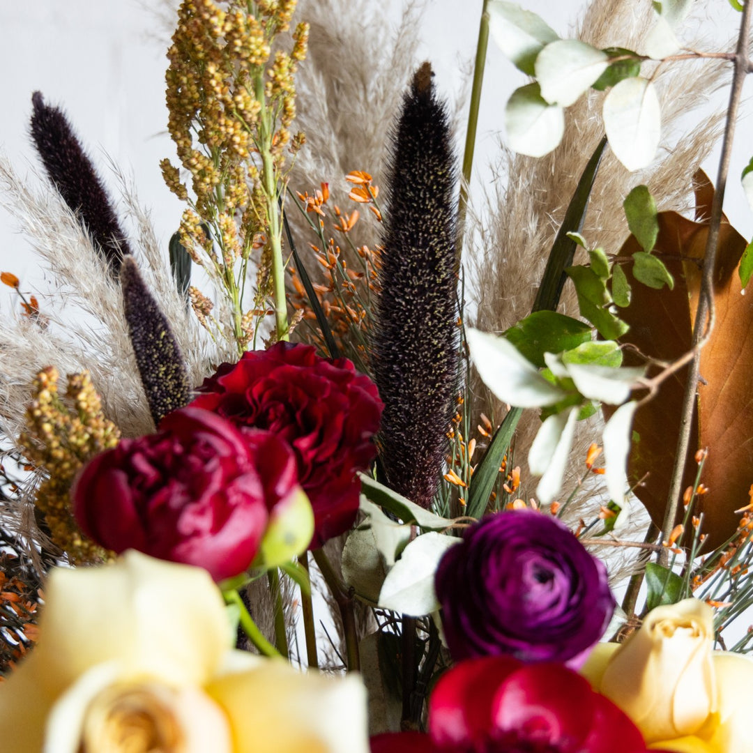 Close-up of a bouquet with red, purple, and yellow flowers, including pampas grass and eucalyptus.