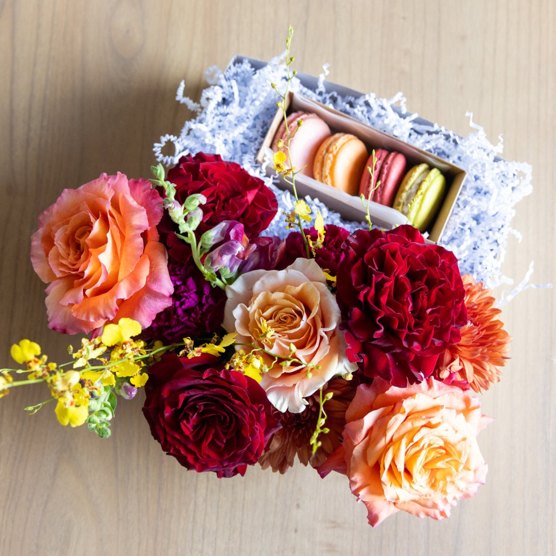 Colorful bouquet of flowers with a box of macarons on a wooden surface