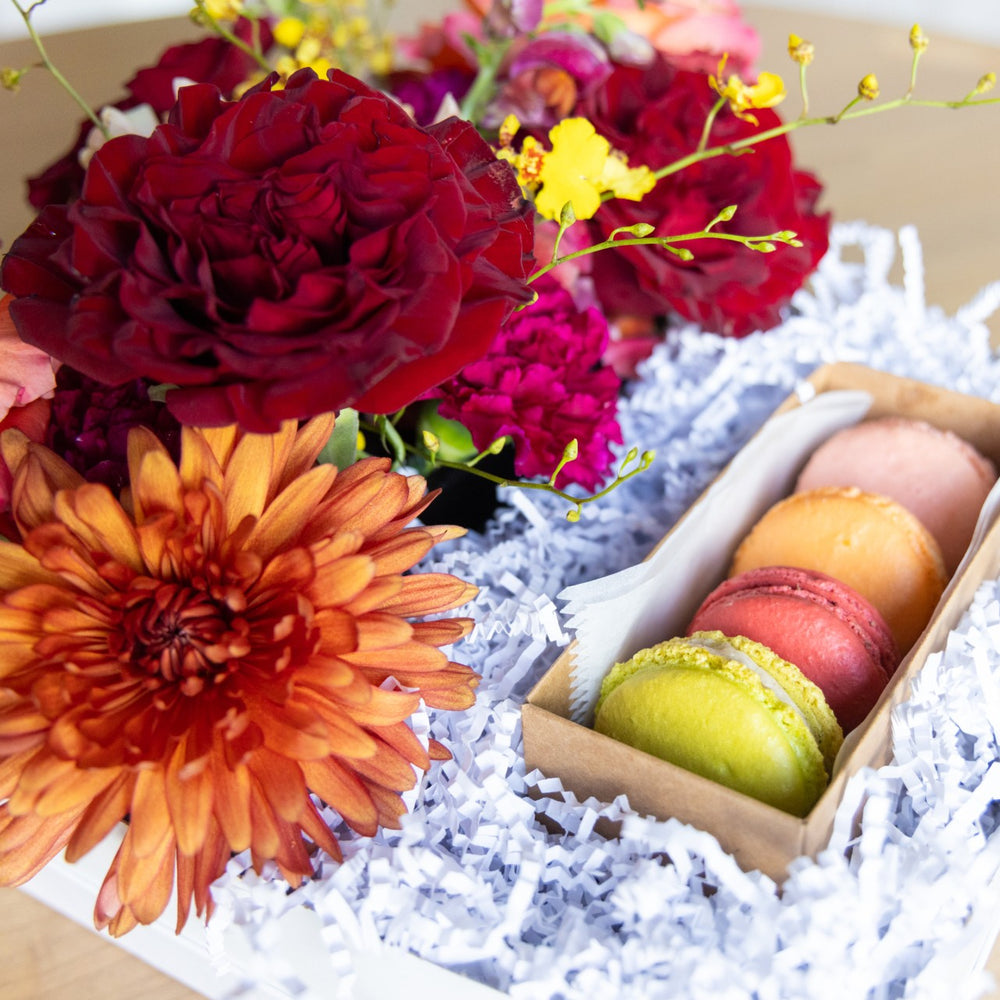 Colorful flowers and macarons in a box with white crinkle paper