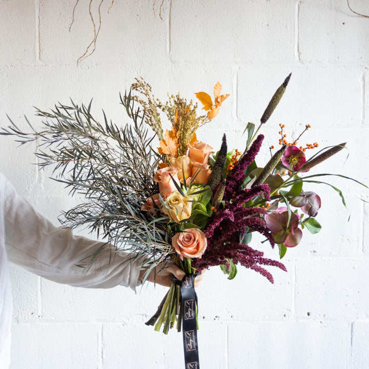 Bouquet of flowers held by a person against a white brick wall