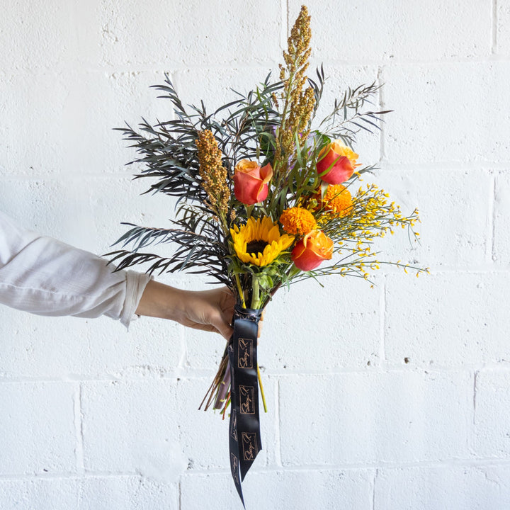 Bouquet of flowers held by a person against a white brick wall