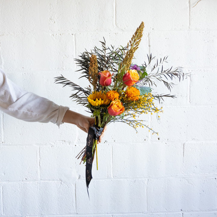 Bouquet of flowers held by a person against a white brick wall