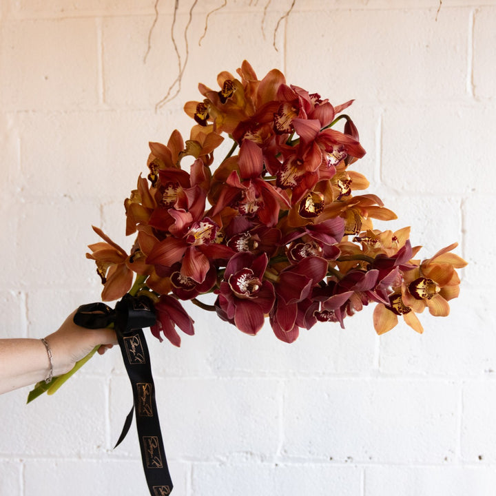 Bouquet of red and orange flowers held against a white brick wall.