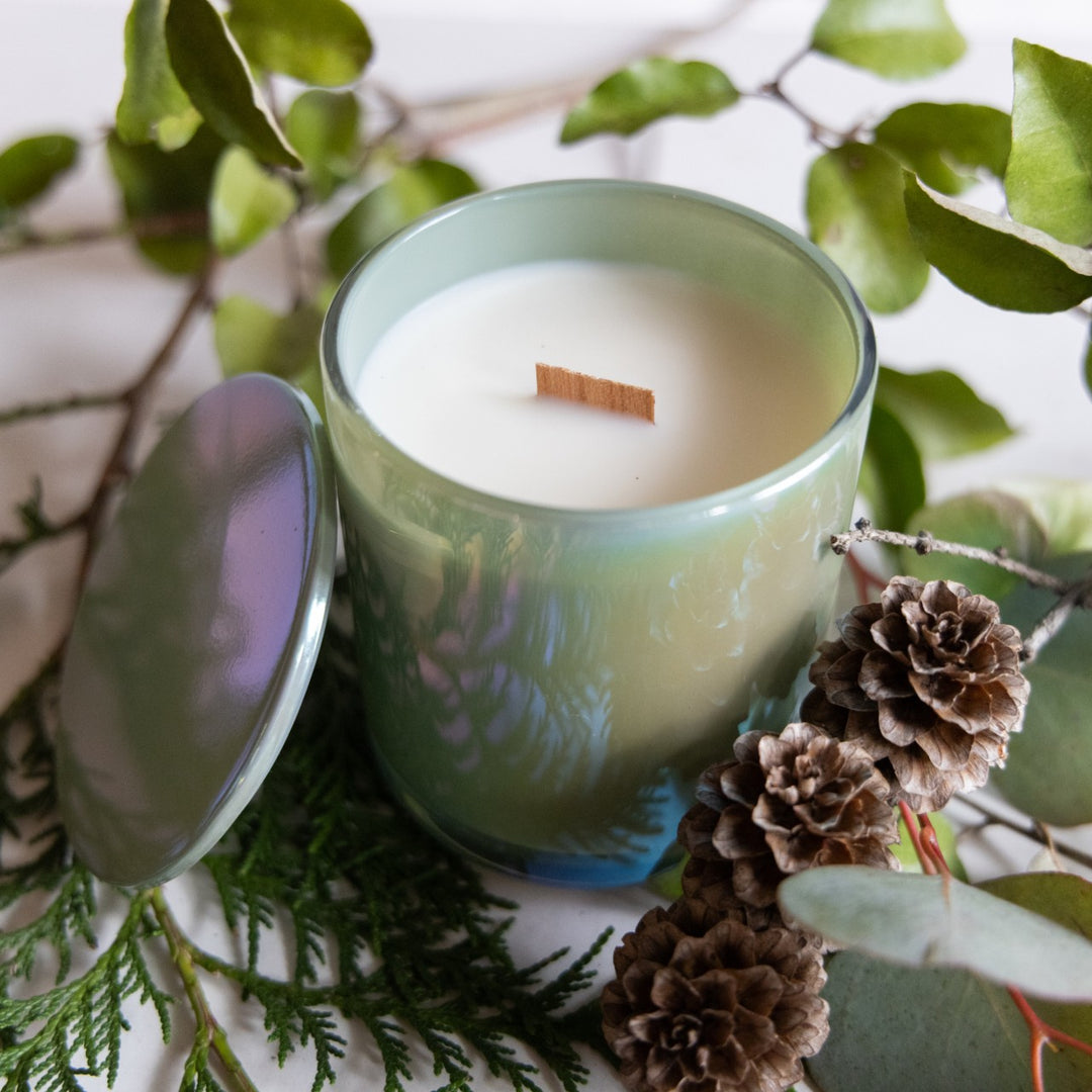 Green candle with a wooden wick surrounded by pine cones and greenery