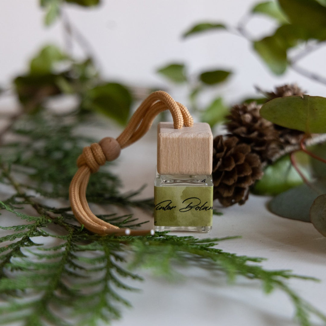 Small bottle of perfume with a wooden holder on a leafy background