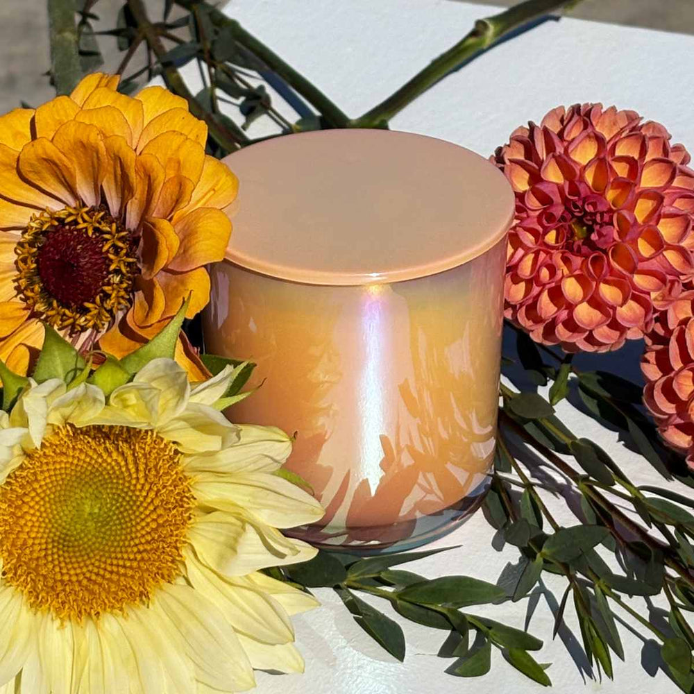 Stacy K Floral | Fleurish Co. | Fall Foliage | Candle with floral arrangement on a reflective surface. Dahlia, zinnia, and sunflower.