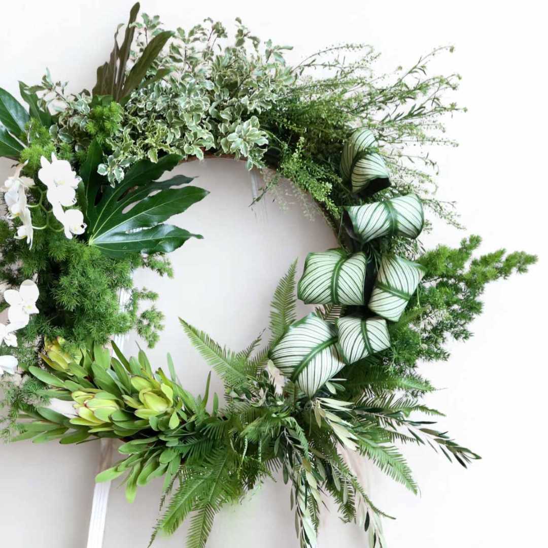 Stacy K Floral | green standing wreath with a variety of greenery and some white florals.