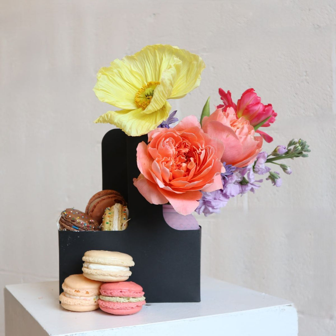 Stacy K Floral | Macaroons and blooms carrier. A black carrier with a bright flower arrangement and fresh macaroons.