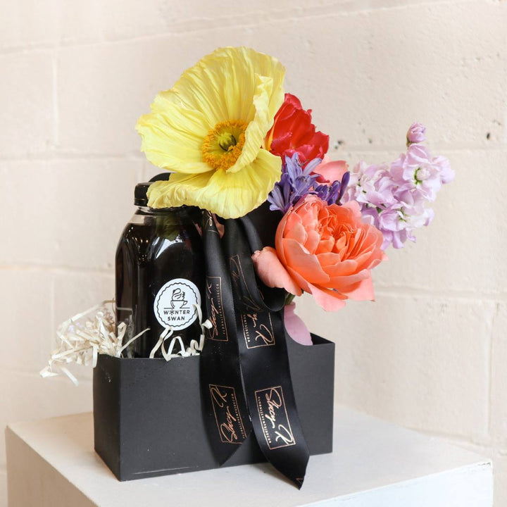 black gift box featuring a stunning arrangement of fresh flowers, including yellow poppy, peach rose, and lilac stock from stacy k floral  paired with a premium cold brew from winter swan coffee