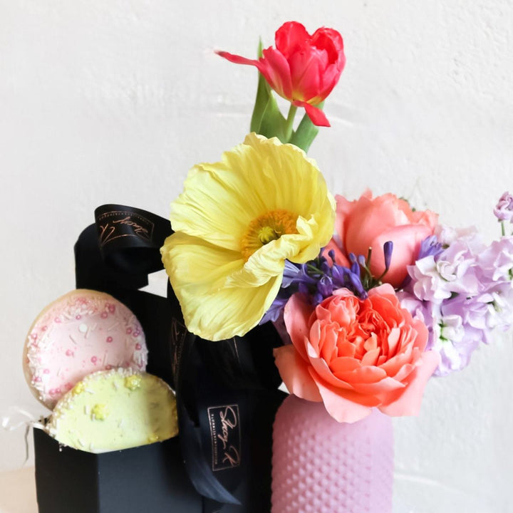 A black carrier filled with an assortment of freshly baked cookies and vibrant, colorful, offering a delightful combination of sweet treats and natural beauty.