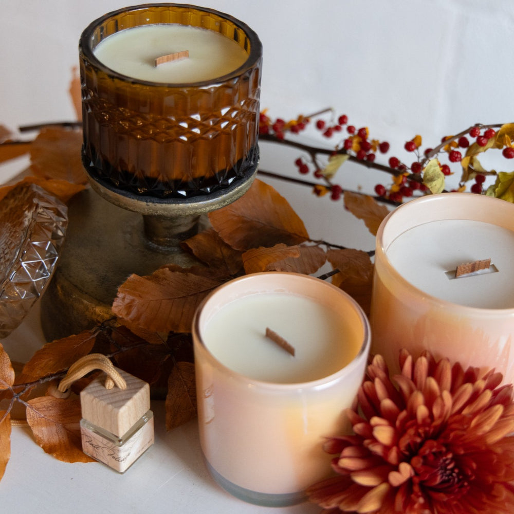 Three candles in glass holders with autumn decorations including leaves and berries on a white surface.