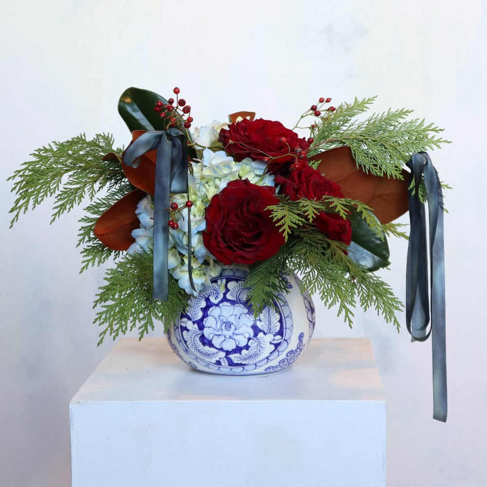 blue and white vase, filled with red roses, evergreen, magnolia, blue hydrangea, red berries and blue silk ribbon.