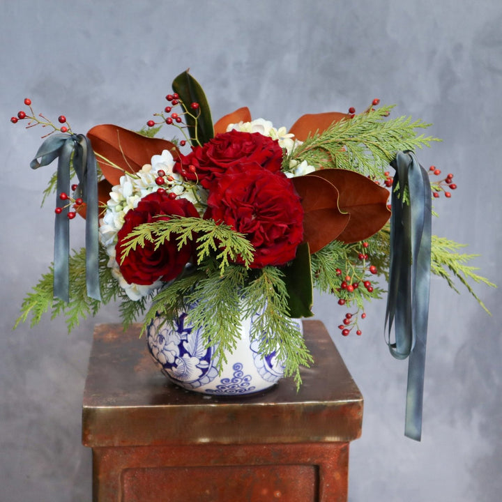 blue and white vase, filled with red roses, evergreen, magnolia, blue hydrangea, red berries and blue silk ribbon.