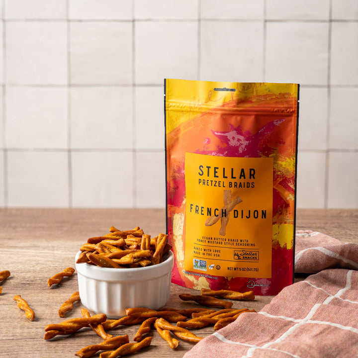 Bag of Stellar Pretzel Brands French Dijon pretzels on a wooden surface with a white bowl and more pretzels.