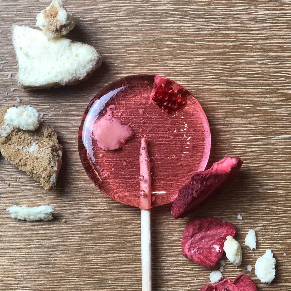 Good Lolli Lollipops | Strawberry Cheesecake | A transparent pink lolli with pieces of strawberry and cheesecake inside.