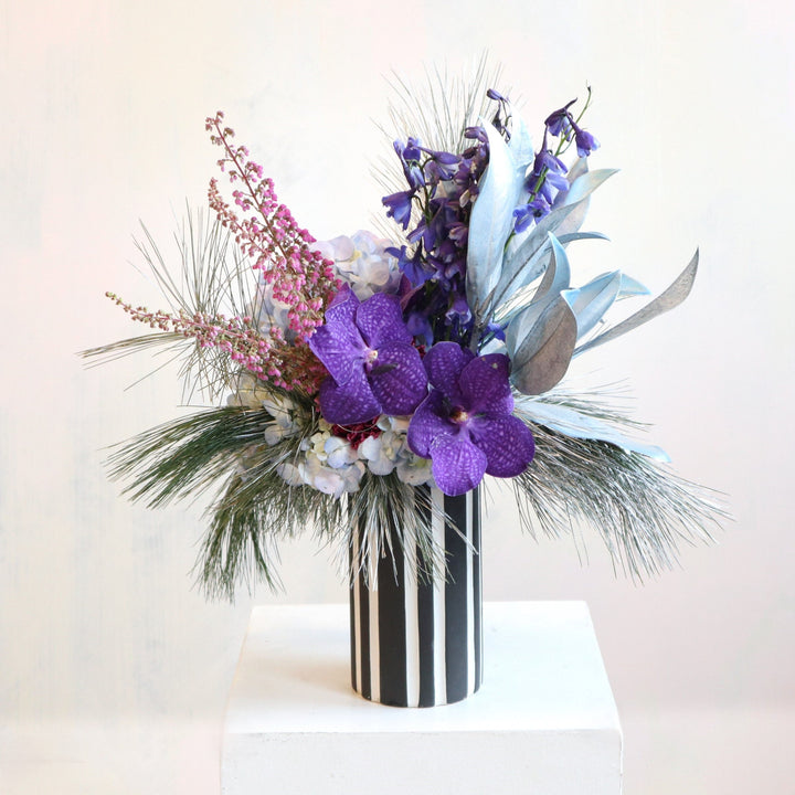 Vased flower arrangement, purple vanda orchids, painted magnolia, blue delphinium, hydrangea, silver white pine. 