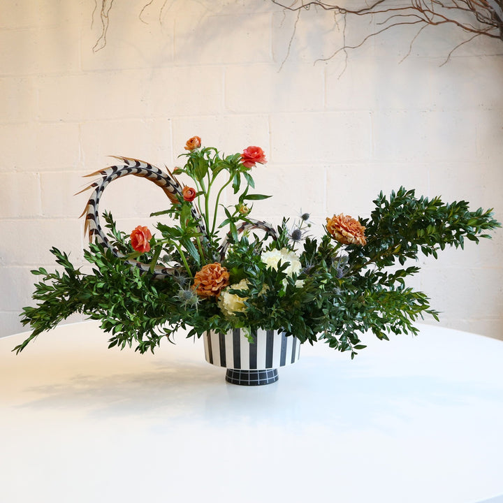 Sublime In Stripes | A vased arrangement with  brown, white, and black coloring, greenery, and florals. Photo taken against a white background. Vase is black and white striped.
