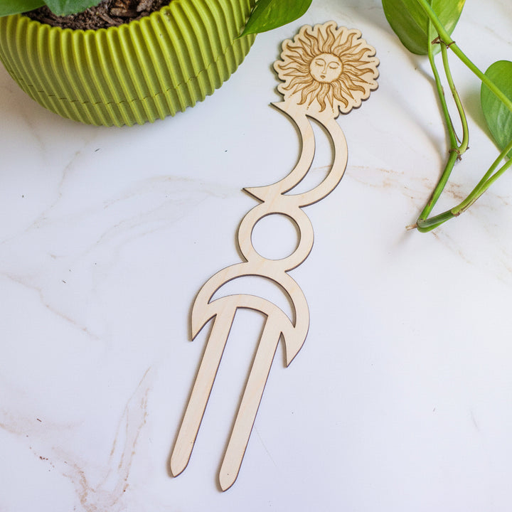 Decorative wooden plant markers with sun and moon designs on a light surface.