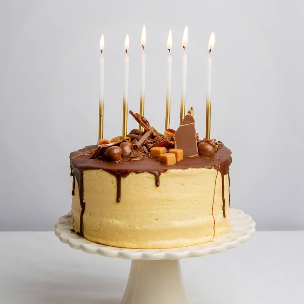 Talking Tables | Chocolate cake with caramel drizzle and lit candles on a white background