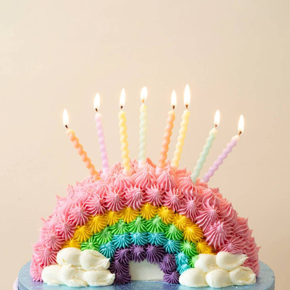 Talking Tables | Spiral Candles | Colorful birthday cake with rainbow frosting and lit candles on a beige background