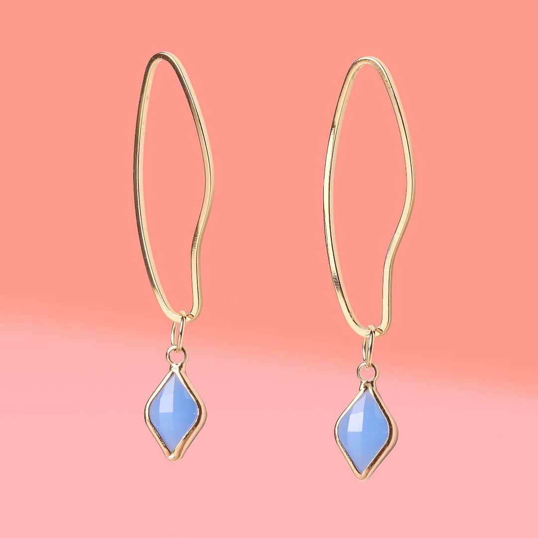 Gold hoop earrings with blue teardrop stones on a pink background
