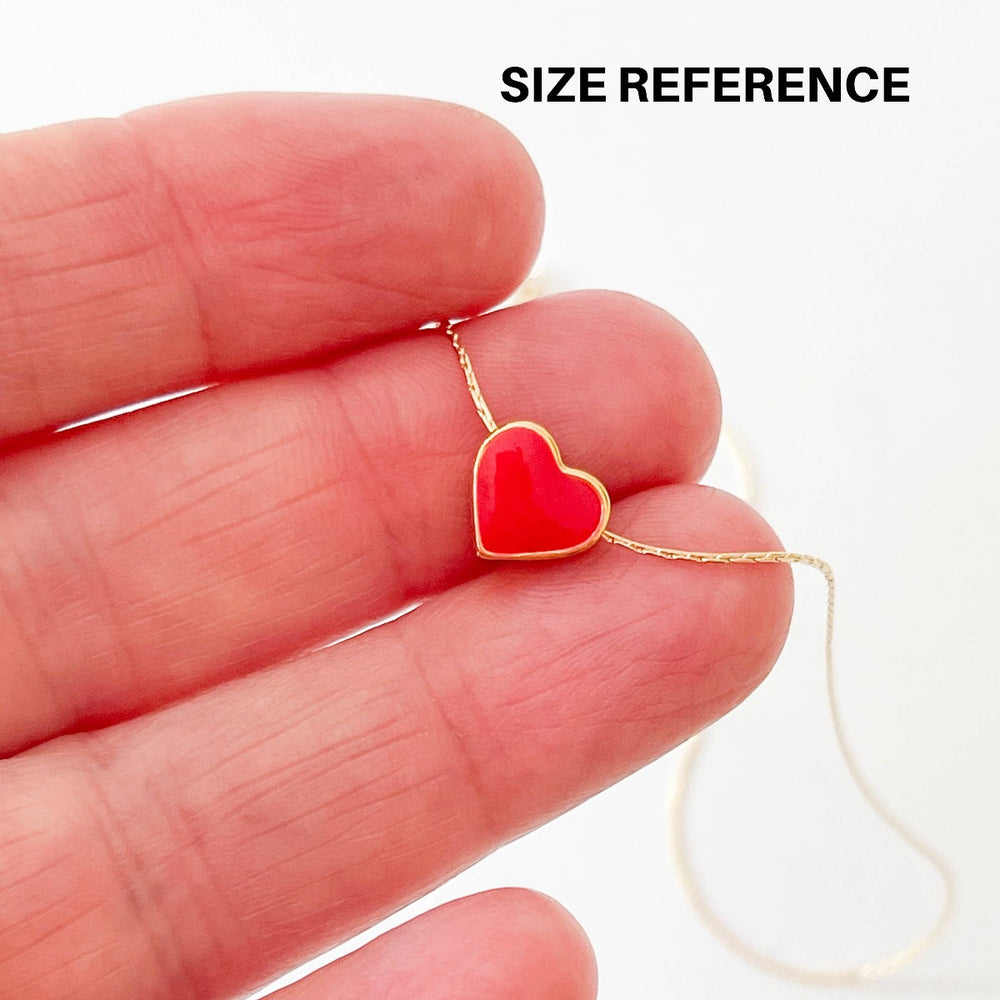 Nest Pretty Things | Tiny Black Heart Charmed Necklace | Close up on a red heart necklace held on a model's hand to demonstrate sizing.