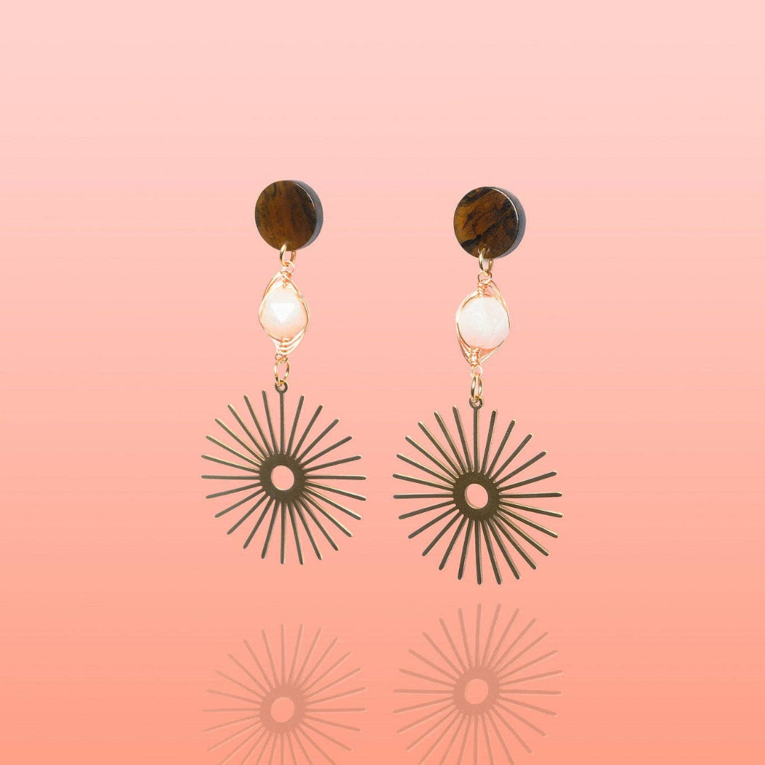 Pair of earrings with sunburst designs on a pink background
