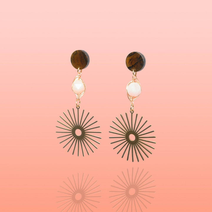 Pair of earrings with sunburst designs on a pink background