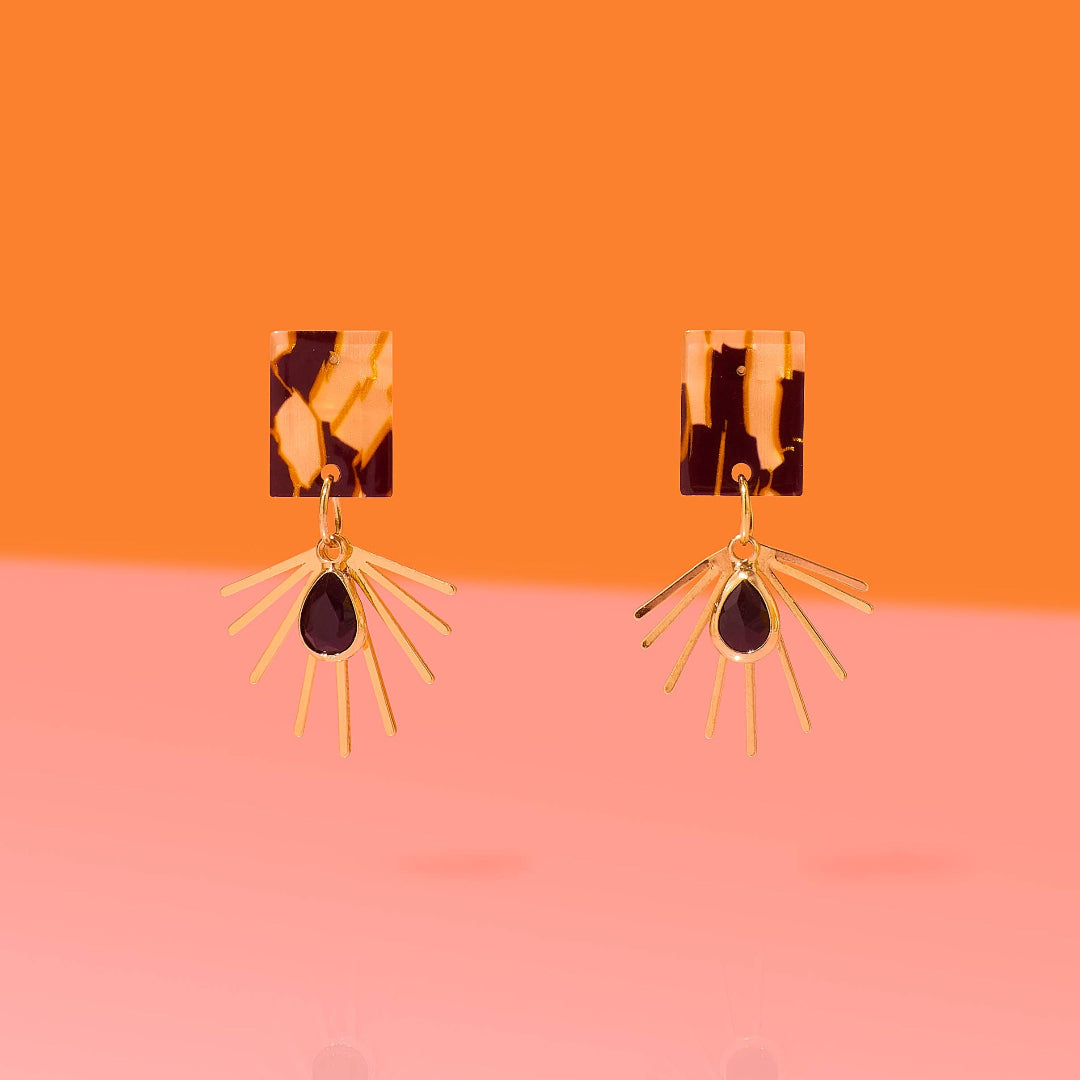 Pair of earrings with tortoiseshell and gold design on an orange and pink gradient background