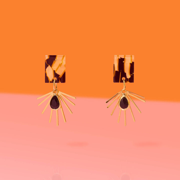 Pair of earrings with tortoiseshell and gold design on an orange and pink gradient background