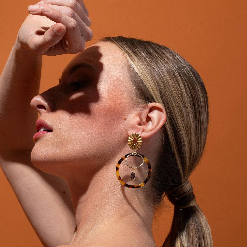 Woman wearing tortoiseshell earrings against an orange background