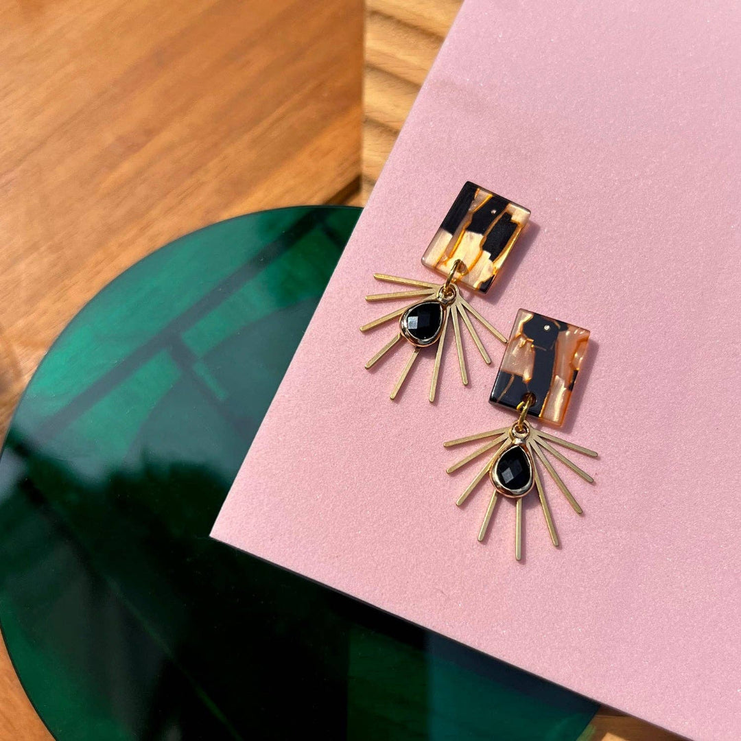 Gold earrings with black and gold accents on a pink surface