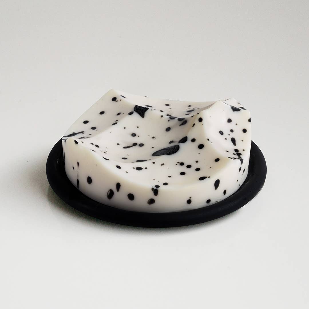 White soap with black specks on a black soap dish against a white background