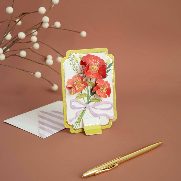Greeting card with floral design on a brown background with a pen and envelope.