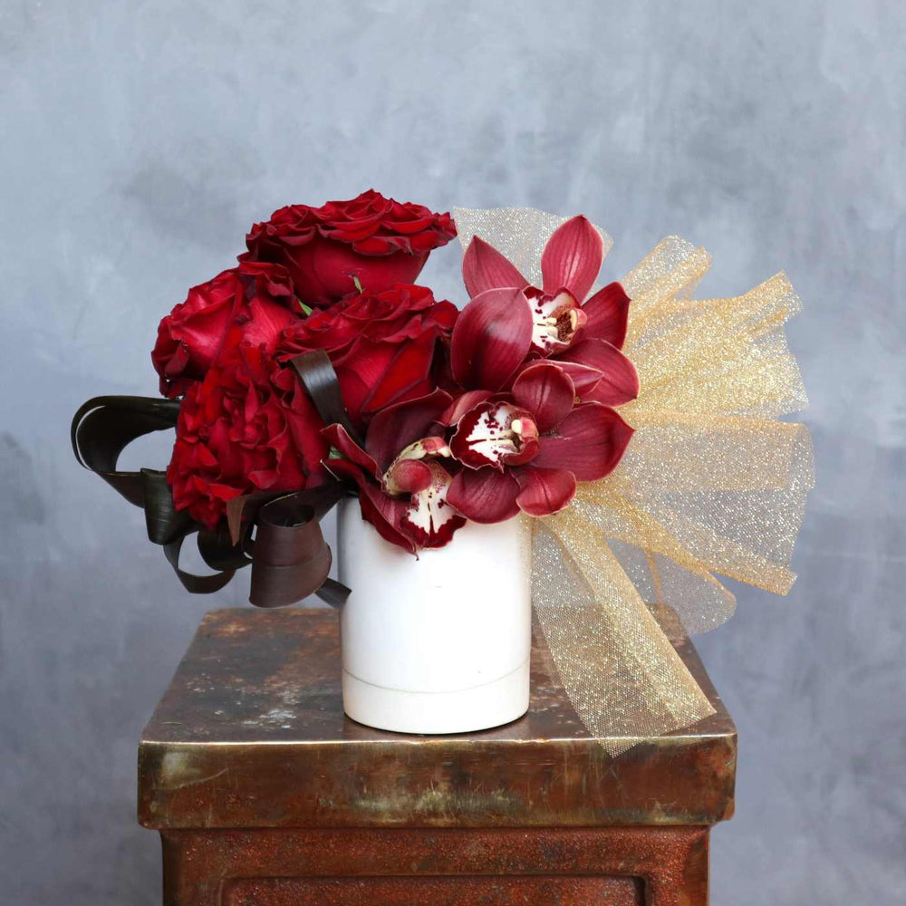 vase with burgundy orchids, red roses, gold tulle and burgundy leaves.