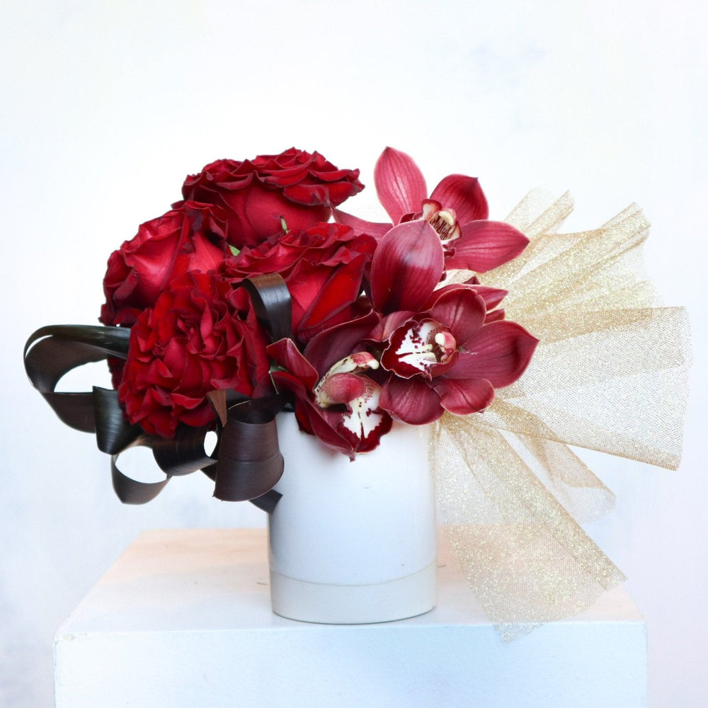 vase with burgundy orchids, red roses, gold tulle ans burgundy leaves.