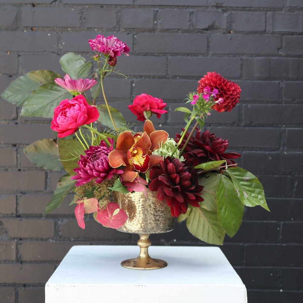 Immerse yourself in the allure of autumn with our stunning moody fall flower arrangement, meticulously crafted to embody the season's rich and dramatic hues. This arrangement features an exquisite combination of garden roses, orchids, fall foliage, mums, and dahlias, all in a palette of deep, sophisticated colors on a dark background.