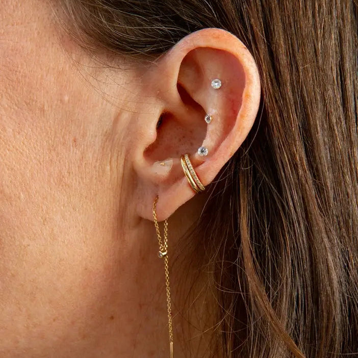 Close-up of an ear with gold earrings and multiple studs.