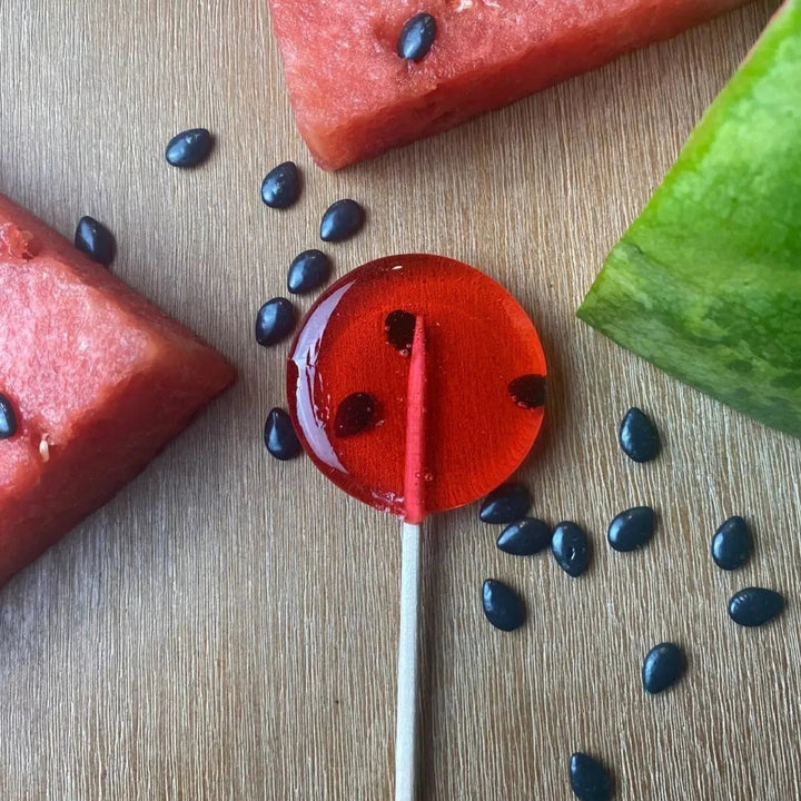 Good Lolli Lollipops | A transparent red lollie with what looks like watermelon seeds on the inside. Photo taken with real watermelon against a wooden background.