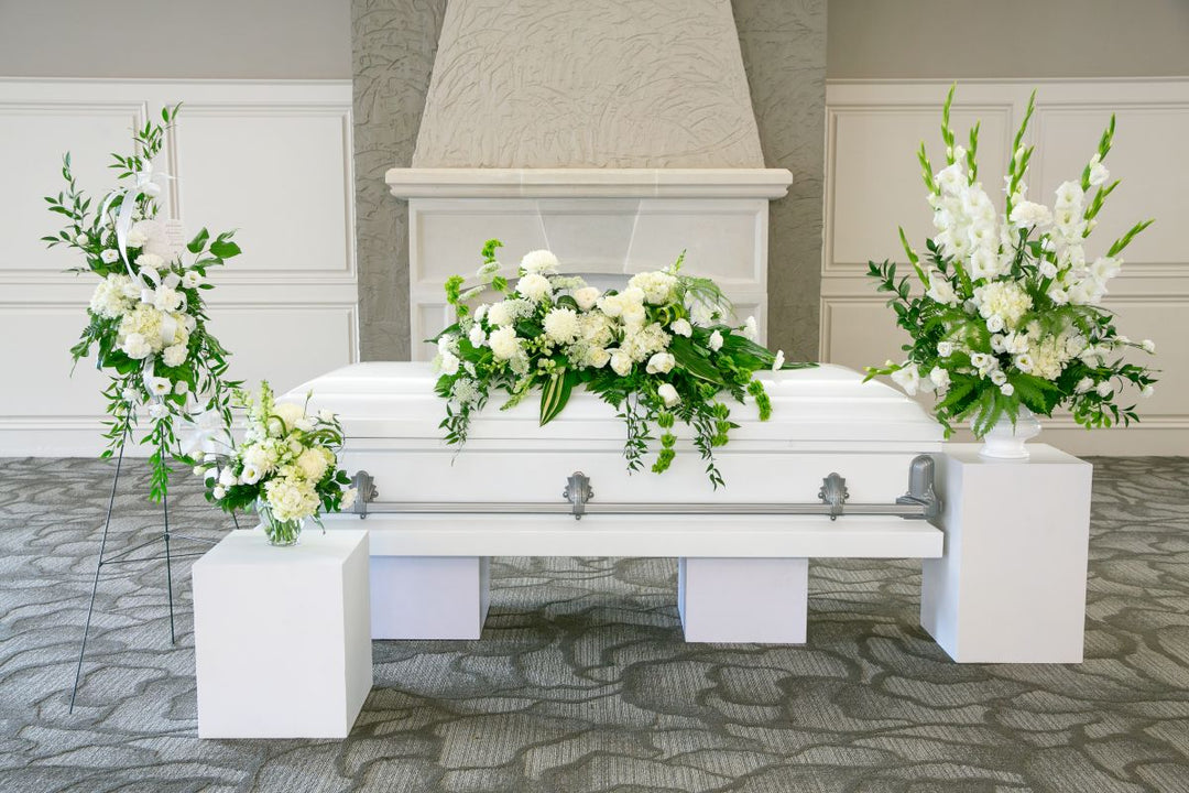 White casket with floral arrangements in a funeral home setting