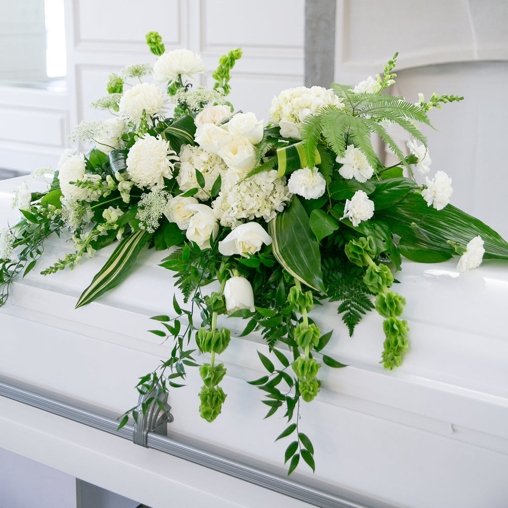 White and green floral arrangement on a white casket