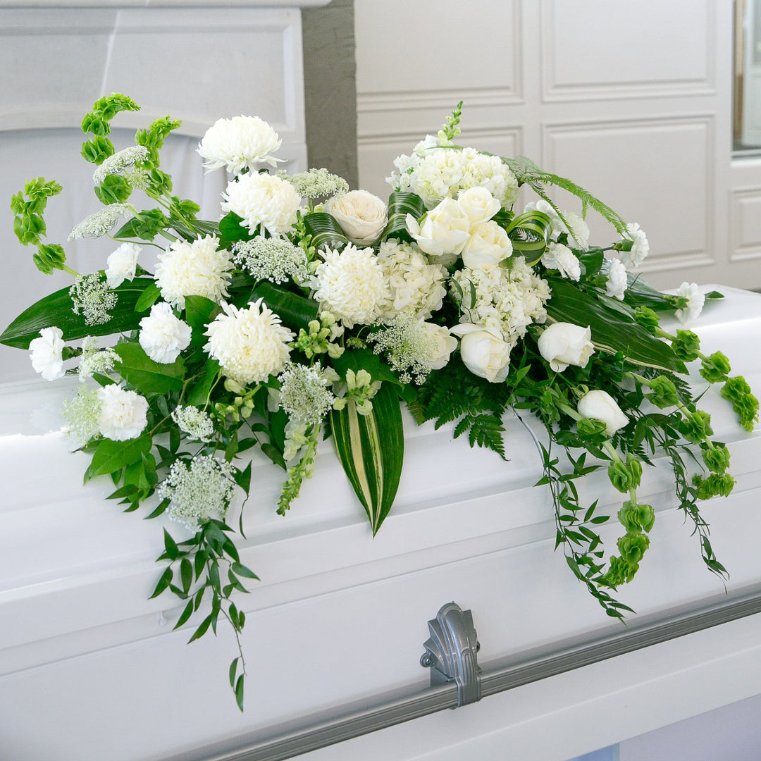 White flowers and greenery on a white casket