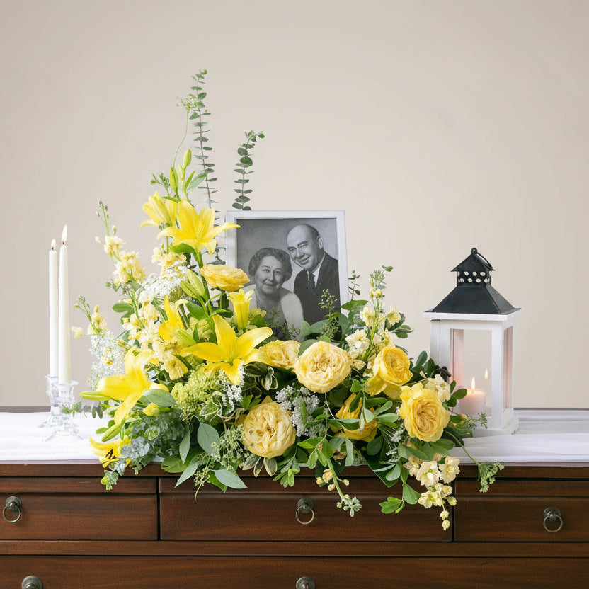Floral arrangement with yellow flowers on a windowsill with a framed photo of an elderly couple.