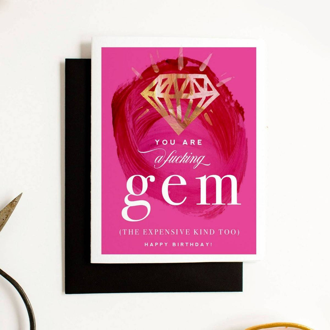 A bright pink card with a gold gem illustration and text that reads "You are a fucking gem (the expensive kind too) Happy Birthday!" Comes with a black envelope. 