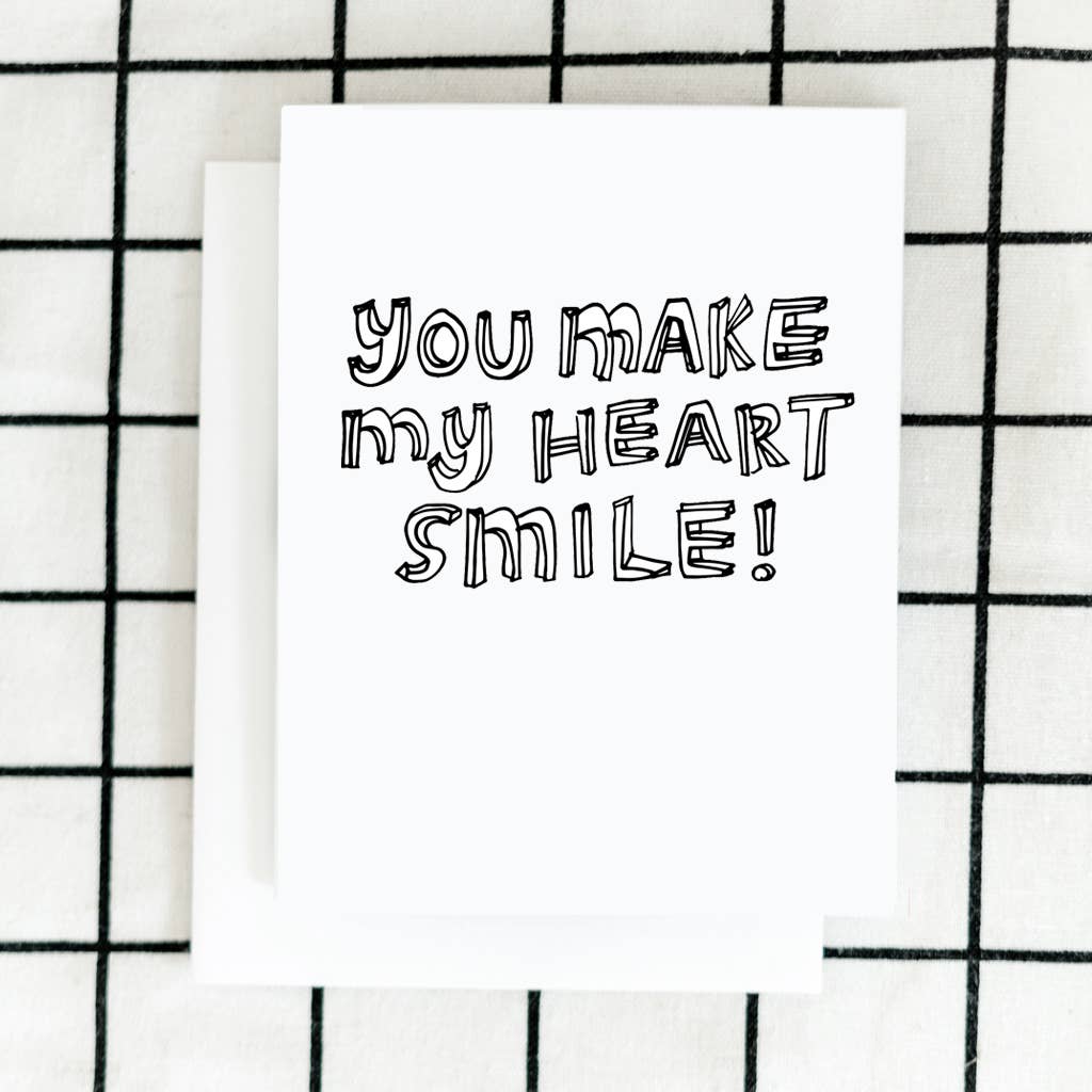 A simple white card with line art text that reads "you make my heart smile!".