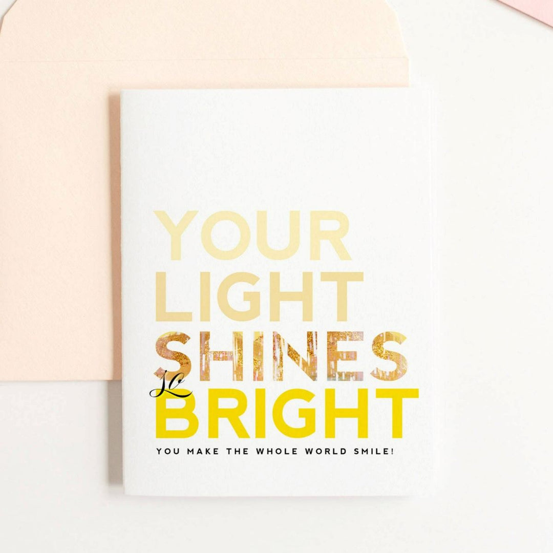 A white card with yellow text that reads "Your light shines so bright, you make the whole world smile!".