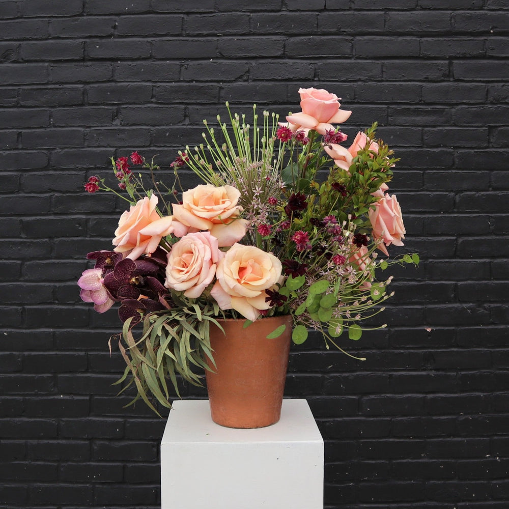Goodness | An earthy summer arrangement with greens, pinks, reds and dark purples. In a copper colored vase. Some flowers pictured are roses and orchids.