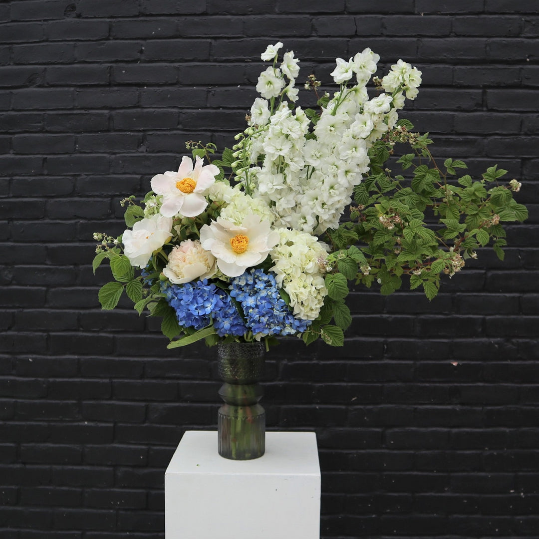 White Swan | A summery arrangement with a focus on asymmetry and the white blooms. Also pictured: Blue hydrangea and berry branches. Arrangement is in a gray tinted semi translucent vase.