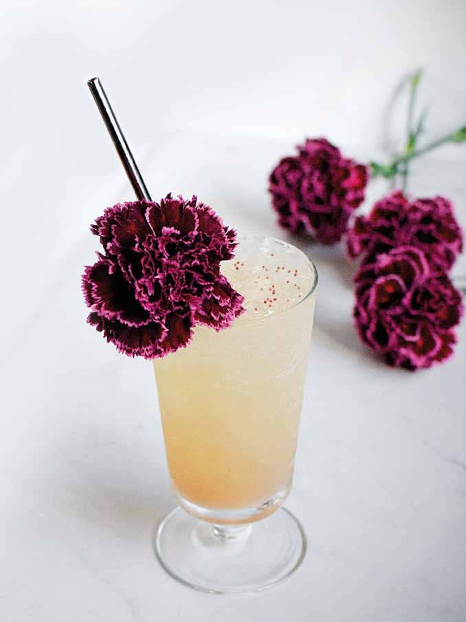 National Book Network | Flower-Infused Cocktail: Flowers, with a Twist | A light peach cocktail with a pink/red flower garnish. Additional flowers lay in the background.