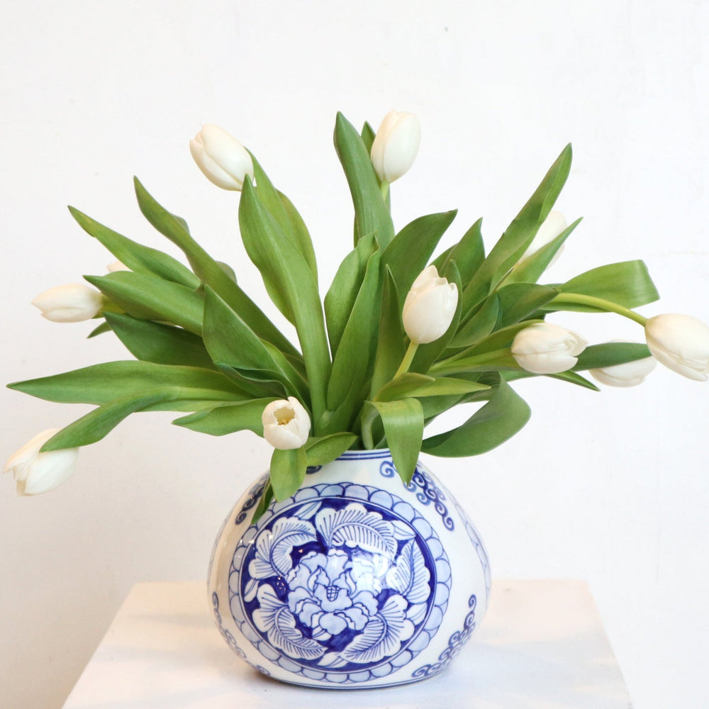 Elegant white tulips in a Delft blue vase on a white pedestal, perfect for home decor or gifting.